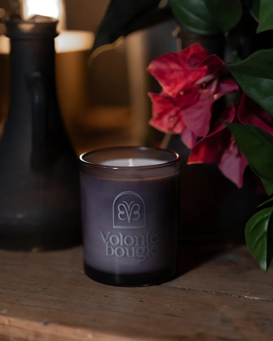 Una vela La Petite junto a flores rojas y un jarrón oscuro