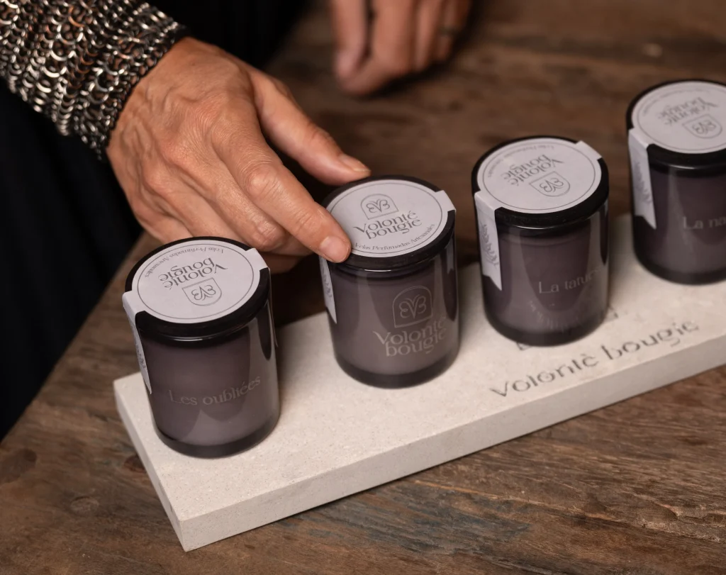 Mano sobre la tapa de una de las velas pequeñas La Petite, en fila sobre una bandeja de piedra grabada con «Volonté bougie»