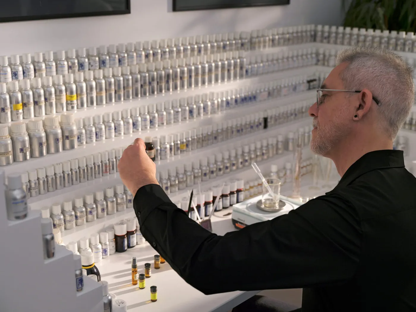 Daniel Josier, perfumista de Volonté Bougie, alcanza un frasco de su órgano de perfumes, de estanterías blancas escalonadas