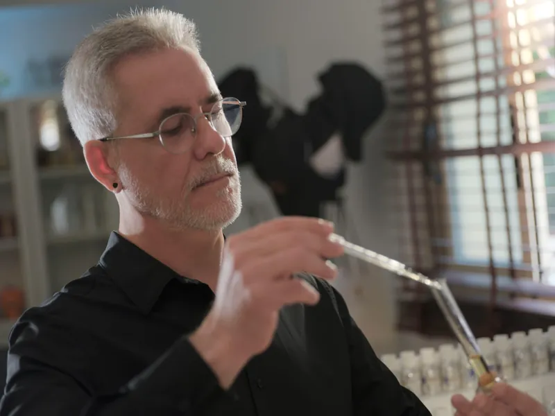 El perfumista sostiene una pipeta de vidrio sobre un vaso de laboratorio