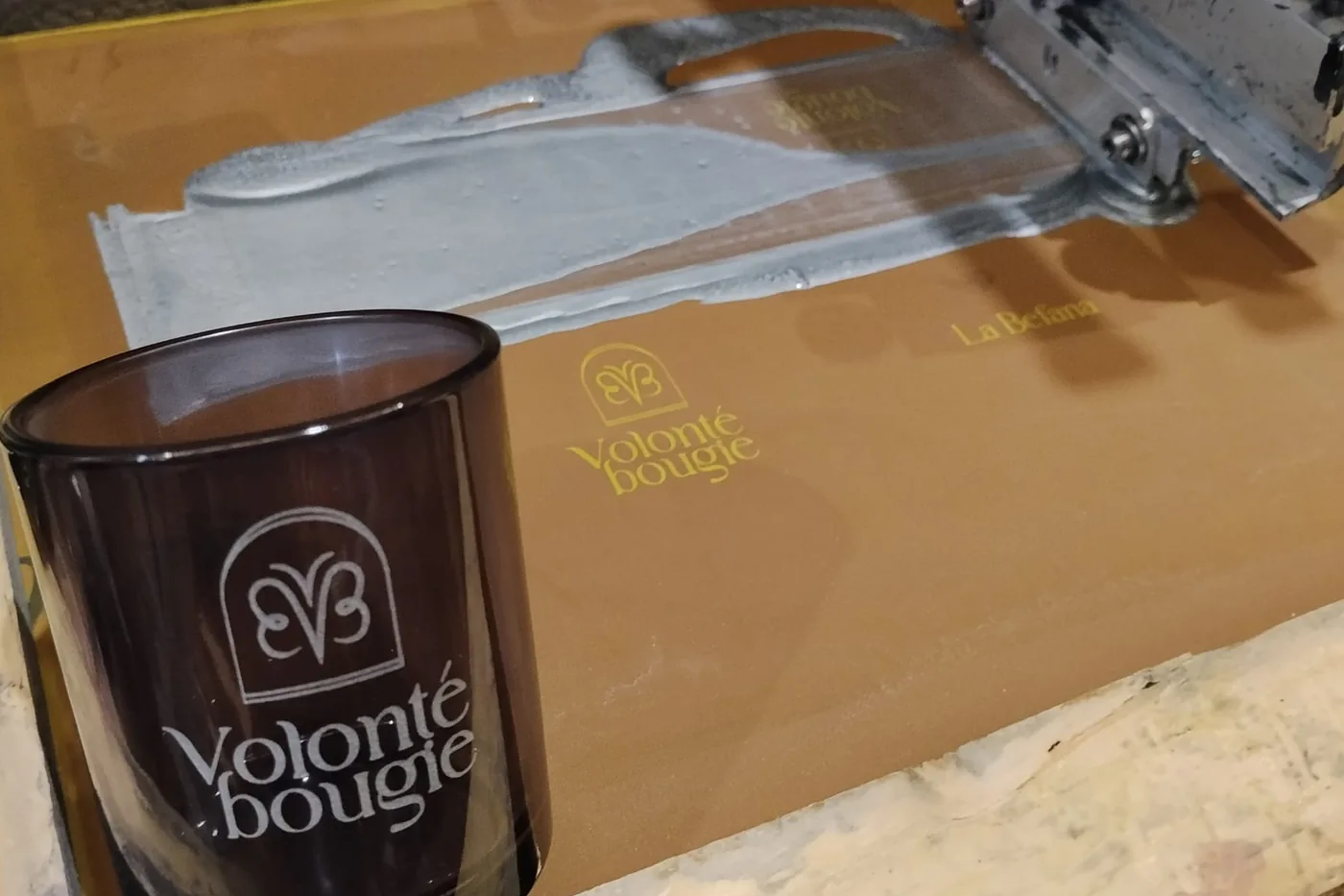 Vaso ahumado con el logotipo ya impreso, apoyado sobre la pantalla de serigrafía junto a la máquina